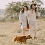 Rodzina z dzieckiem spaceruje z brązowym psem po słonecznej łące