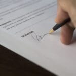 Dłoń podpisująca umowę długopisem na drewnianym biurku