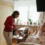 Opiekun podaje herbatę seniorce w przytulnej sypialni, troskliwa opieka