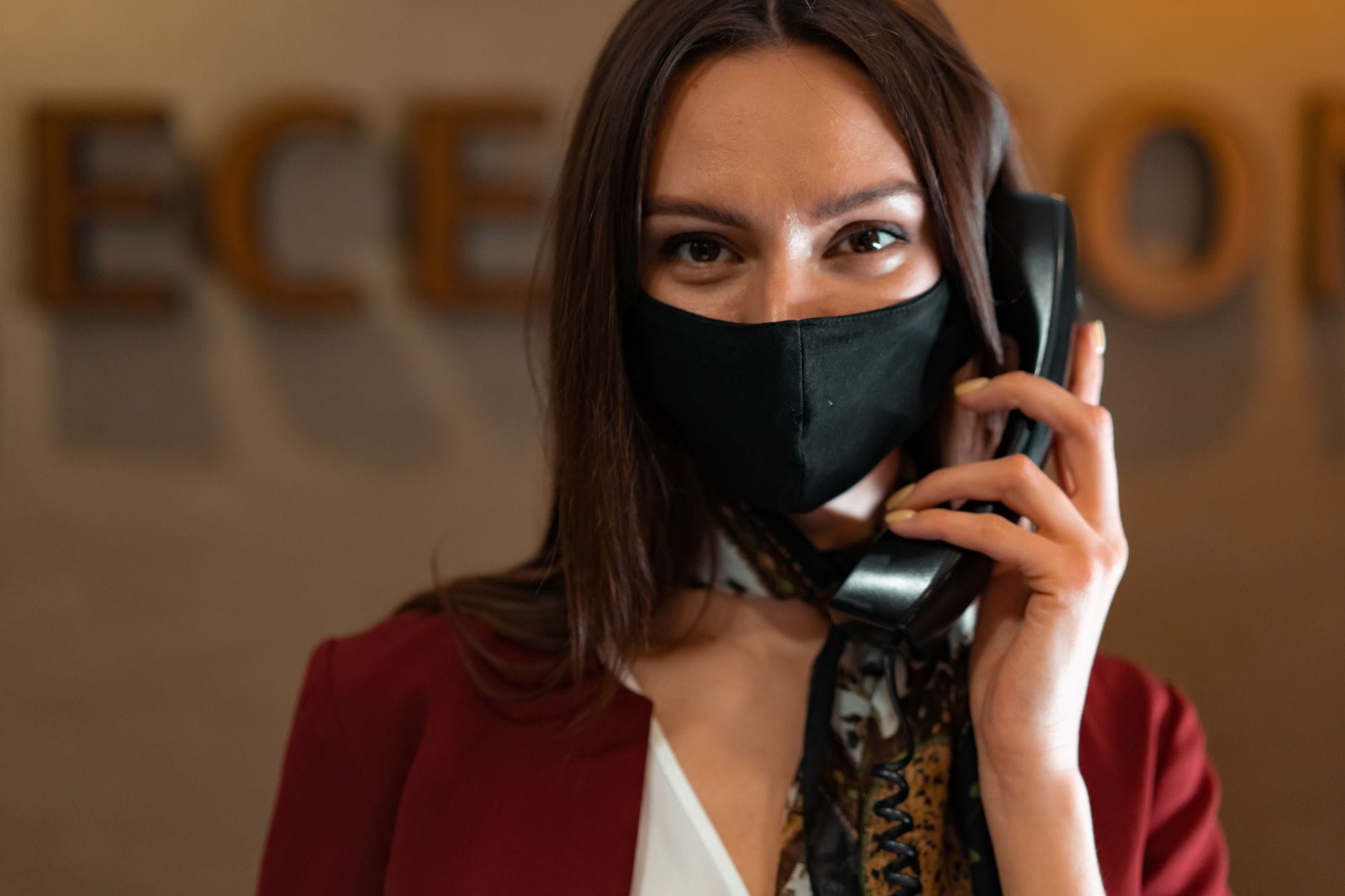 Recepcjonistka w maseczce rozmawia przez telefon przy hotelowej ladzie