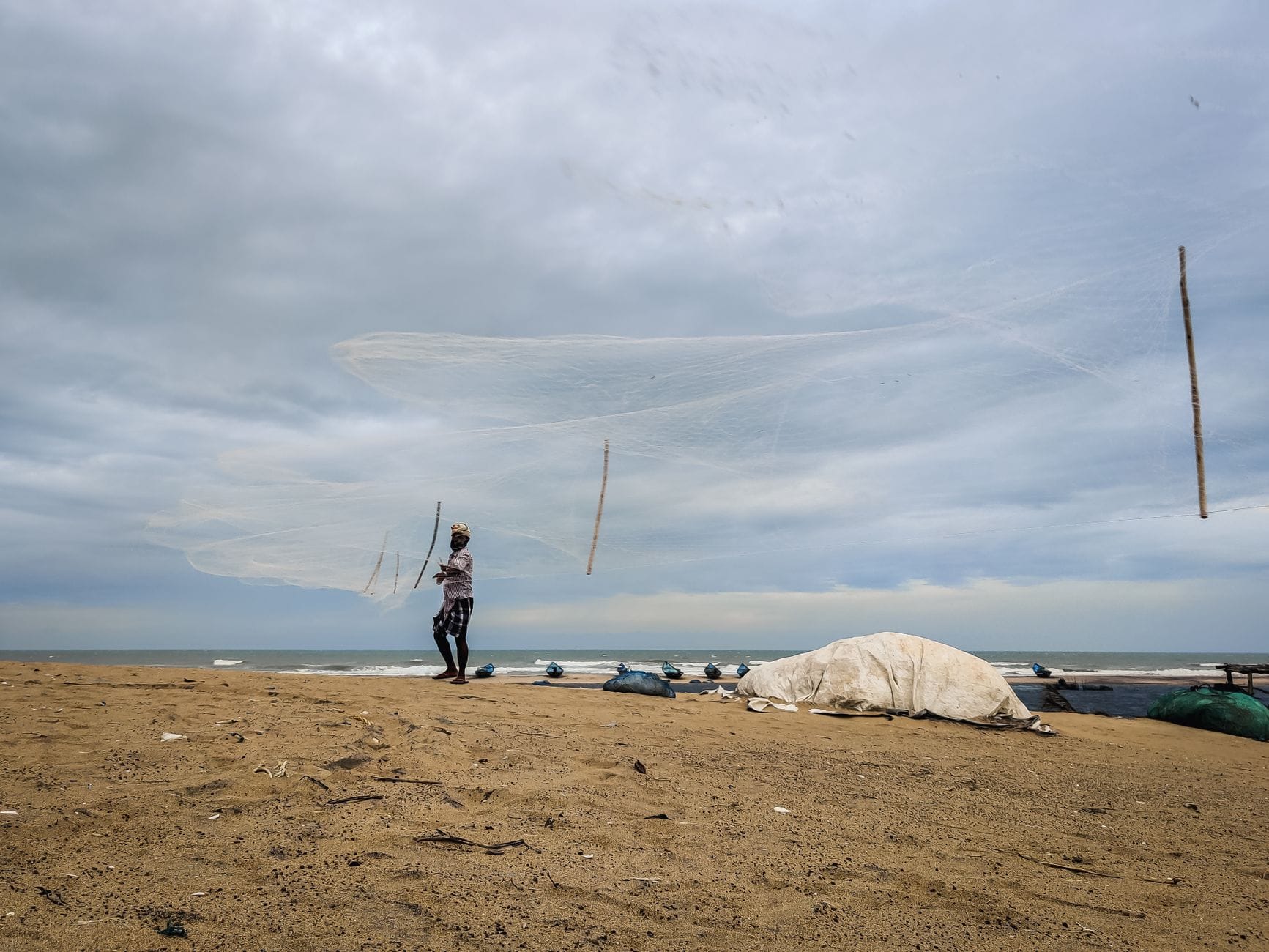 Rybak zarzucający sieć na piaszczystej plaży w Indiach pod zachmurzonym niebem